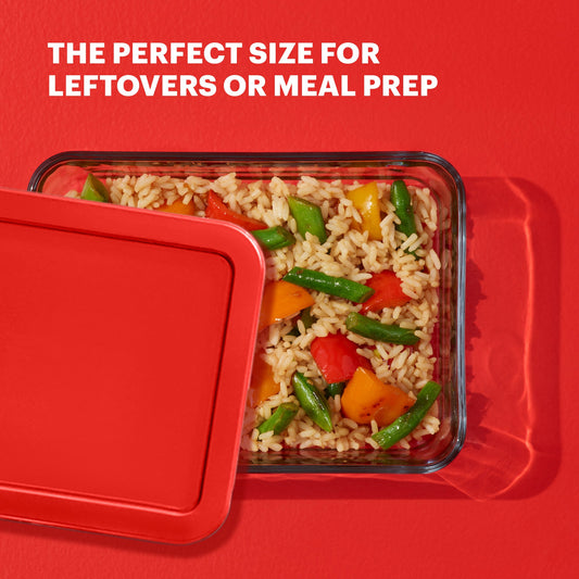 Glass food container with lid filled with rice and vegetables on a red background