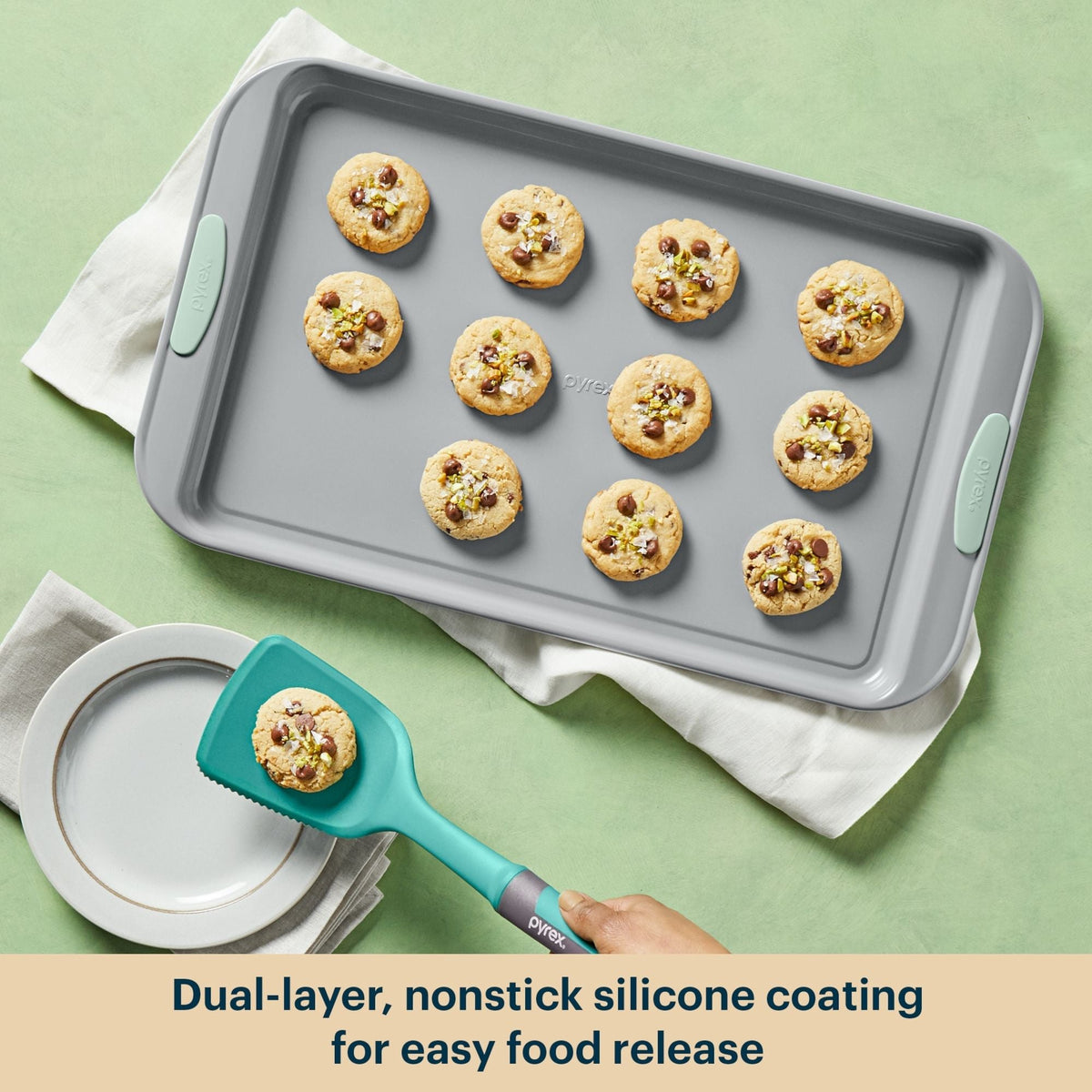 Gray baking tray with cookies and a teal spatula on a green background