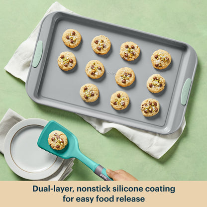 Gray baking tray with cookies and a teal spatula on a green background