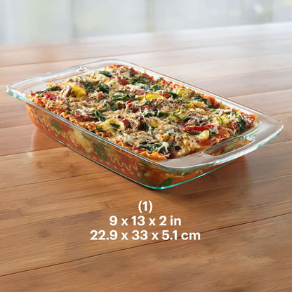 Glass baking dish with a lasagna on a wooden table, showing dimensions.