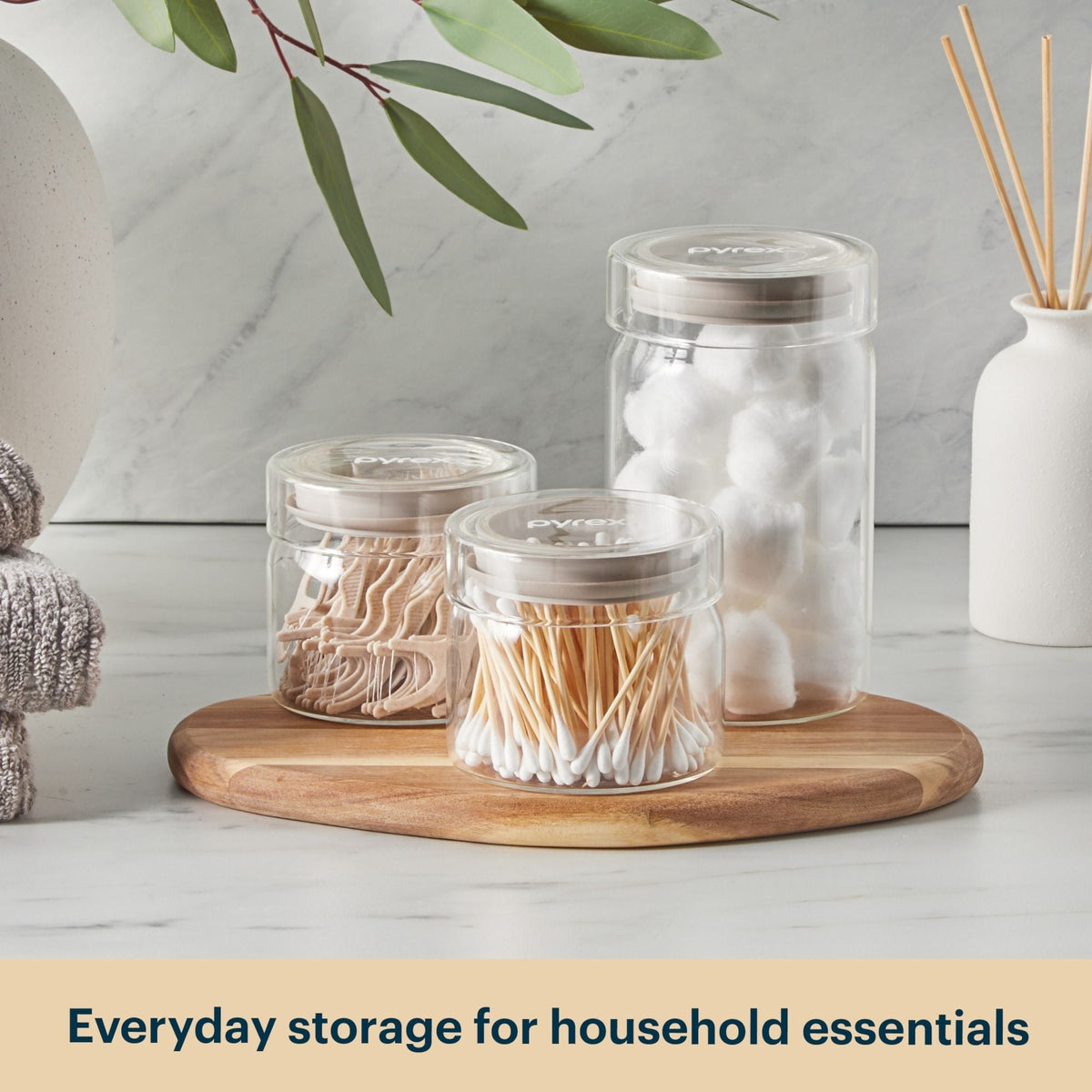 Clear jars with household essentials on a wooden tray with a neutral background